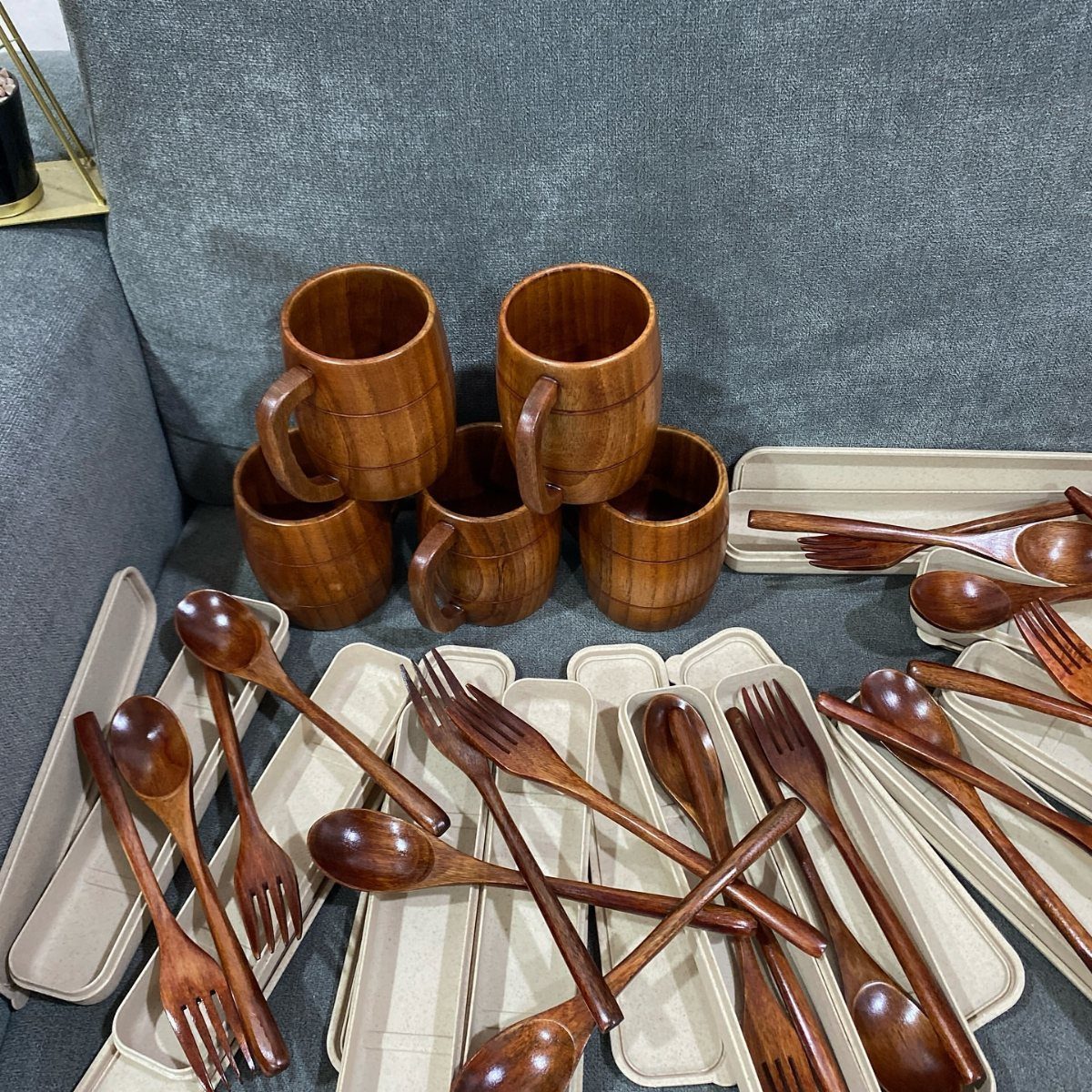 Wooden mugs and matching wooden cutlery set on a grey fabric background.