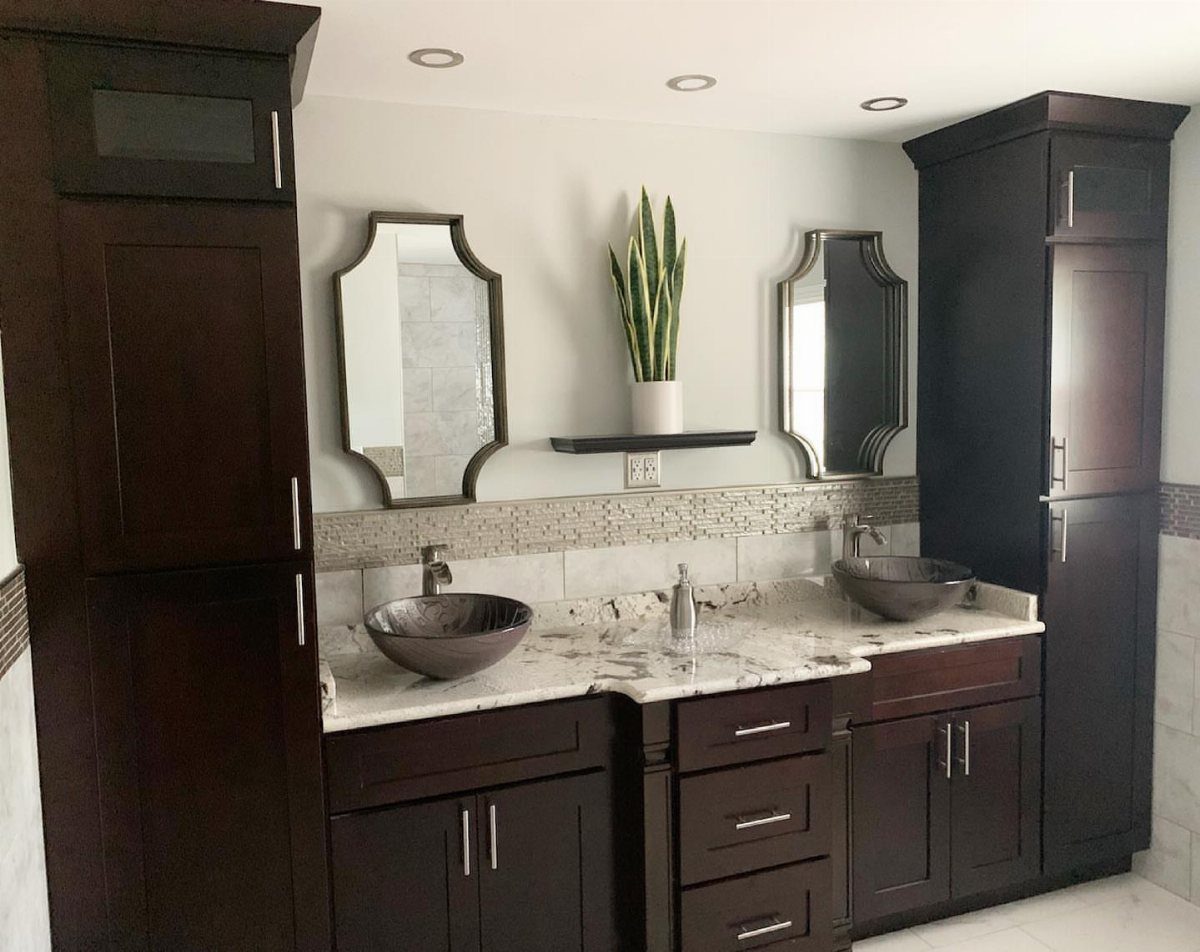 Dark brown bathroom cabinets with white marble countertops and two vessel sinks.