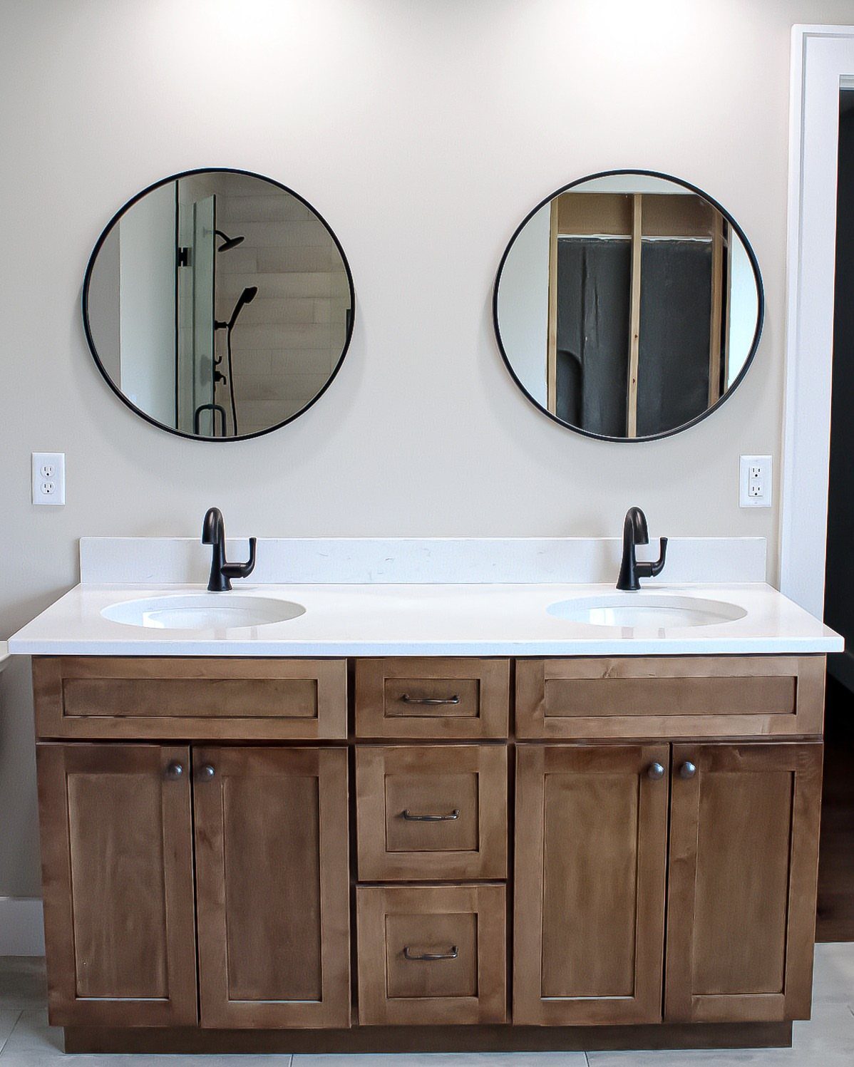 Brown wooden bathroom vanity with white quartz countertops and two round black mirrors.