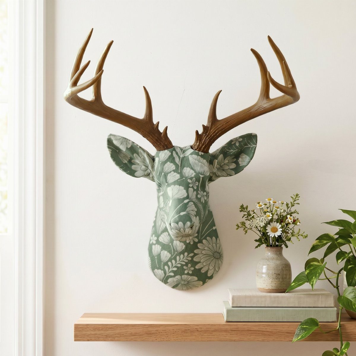 Floral patterned faux deer head mount on a white wall above a wooden shelf.