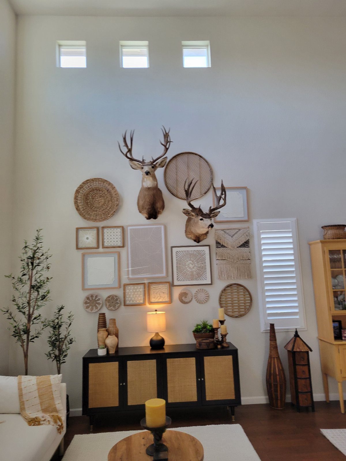 Deer head mounts and woven baskets in a layered wall decor arrangement above a sideboard.