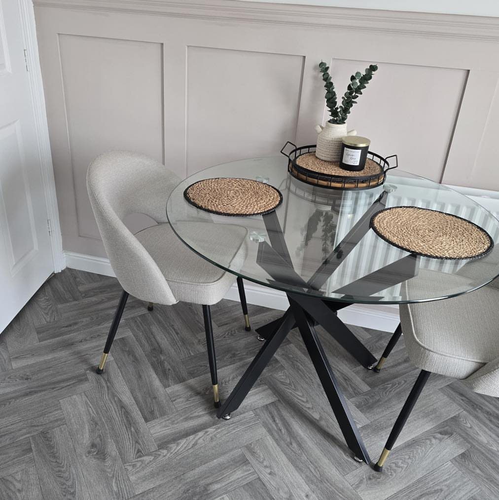 Round glass dining table with black legs and grey chairs in a modern room.