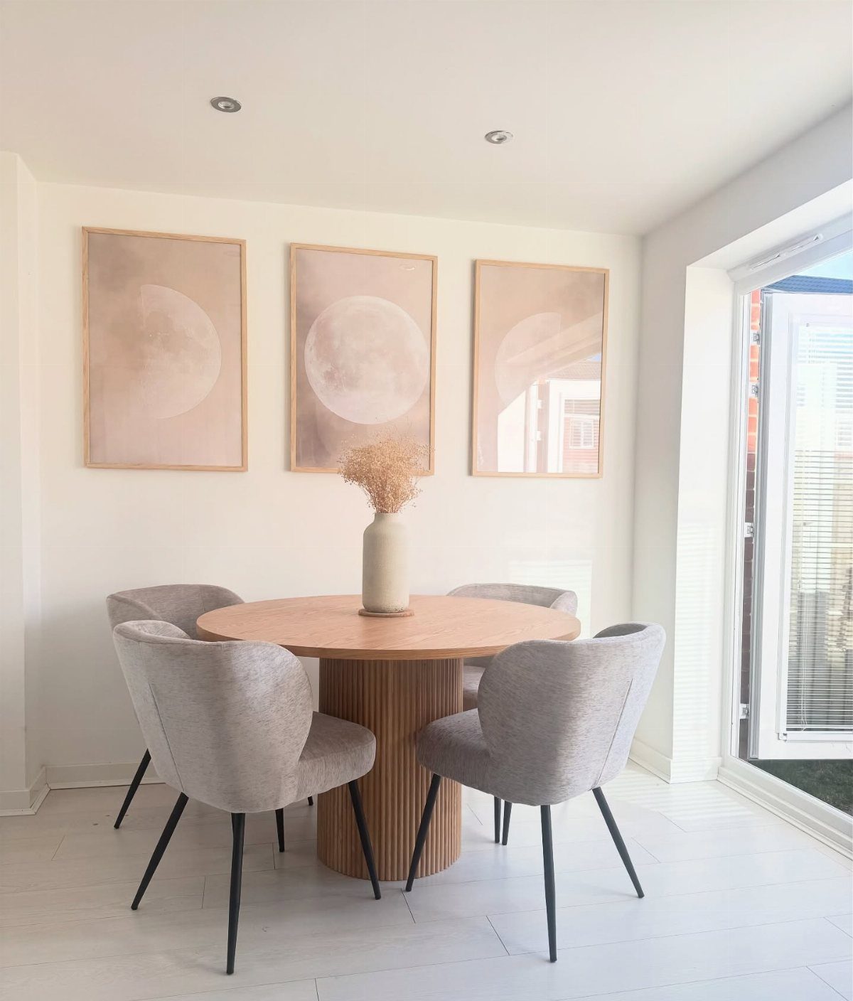 Round wooden dining table with a fluted pedestal base and grey upholstered chairs.