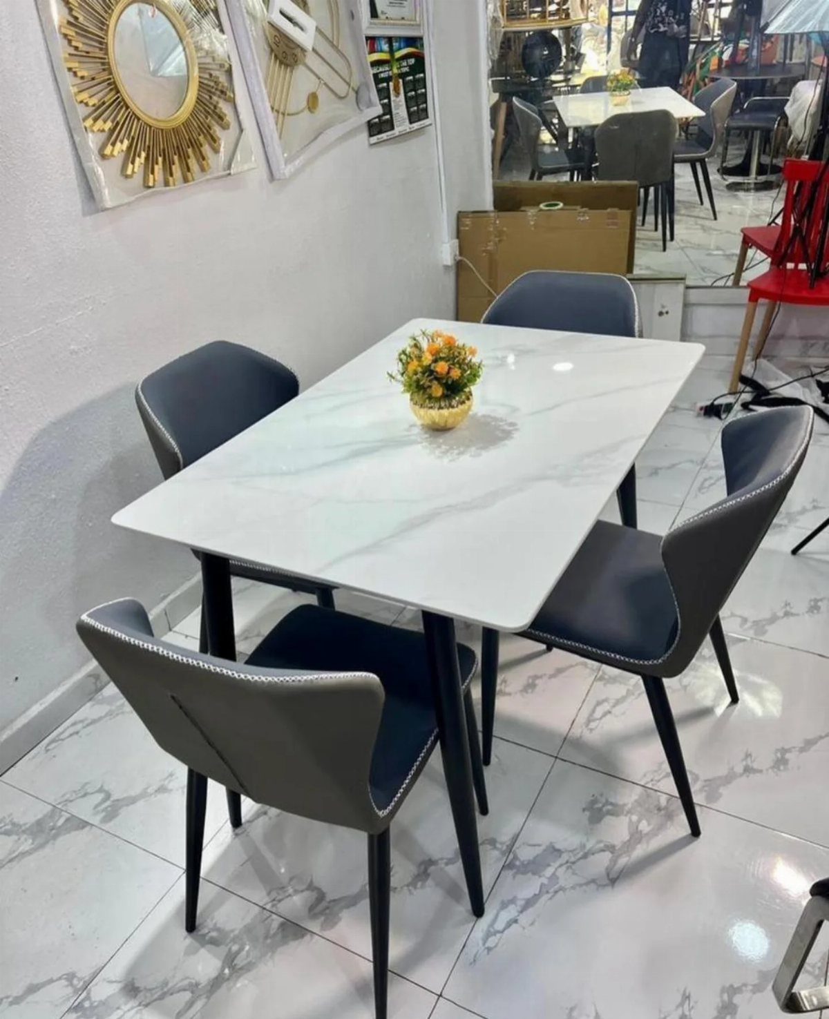 Rectangular white marble dining table with four grey chairs and a small floral centerpiece.