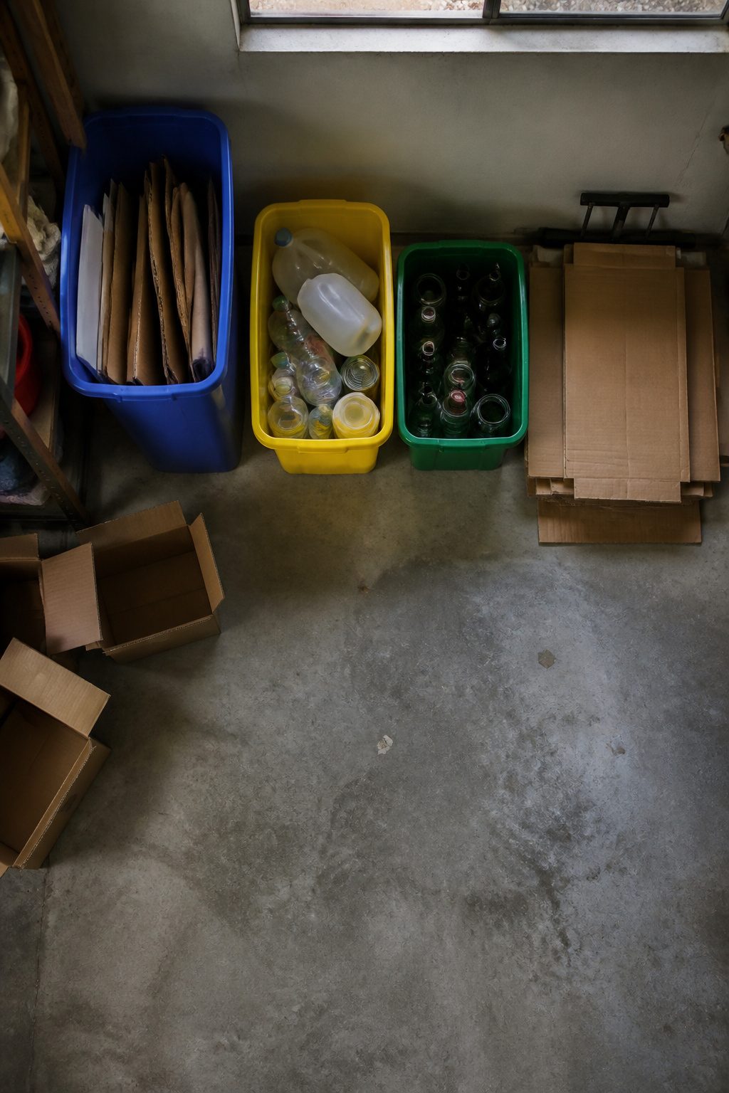 Three bins organized for recycling paper, plastic, and glass in a garage.