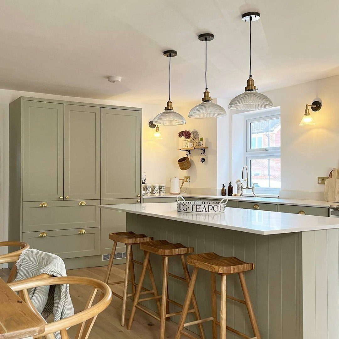 Farmhouse Kitchen Island Ideas: 14 Styles with Photos 14 Three glass pendant lights hanging over a sage green farmhouse kitchen island with stools.