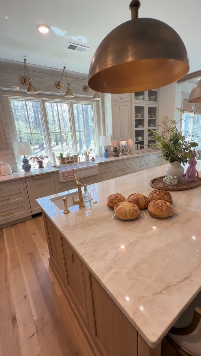 Farmhouse Kitchen Island Ideas: 14 Styles with Photos 10 Light stone kitchen island with bread rolls and a copper pendant light above.