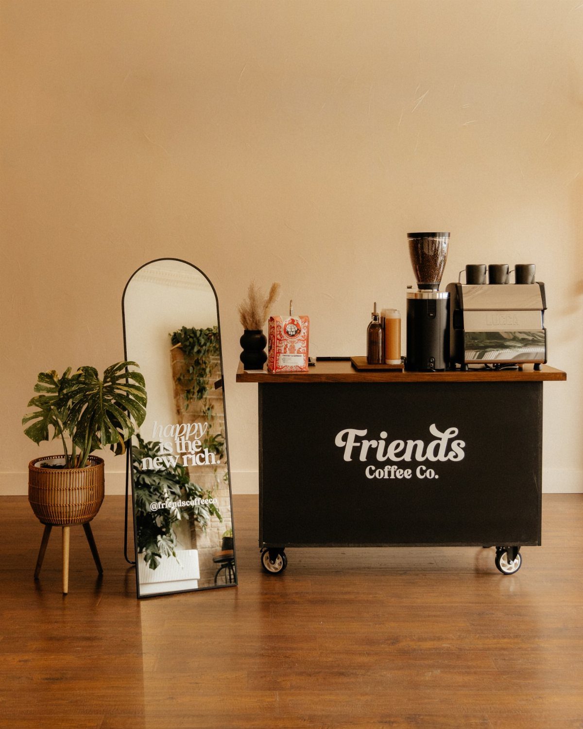 16 Home Coffee Stand Ideas to Fit Any Space 10 Black mobile coffee cart with wooden top, espresso machine, and Friends Coffee Co. branding.