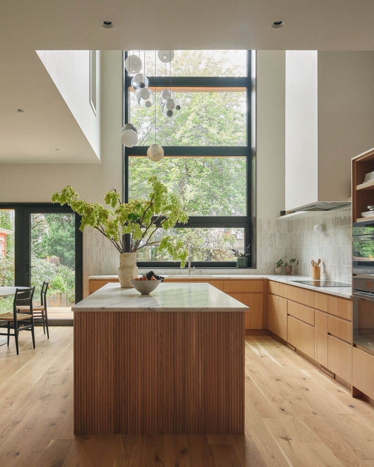 20 Home Kitchen Decor Ideas to Refresh Your Space 18 Modern kitchen with double-height ceilings and large clerestory windows overlooking lush green trees.