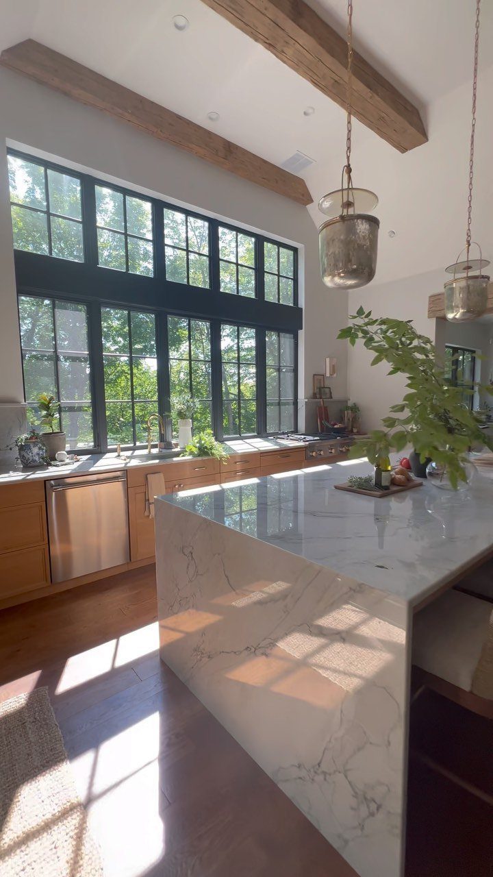 20 Home Kitchen Decor Ideas to Refresh Your Space 17 Bright kitchen with a large black-framed window casting sunlight onto a white marble island.