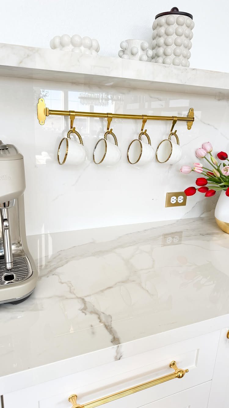 White coffee station with marble countertops, gold mug rail, and silver espresso machine.