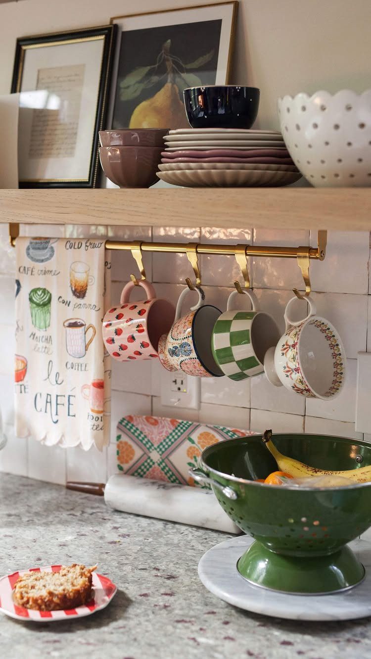 Colorful patterned mugs hanging from a gold rail beneath a wooden kitchen shelf