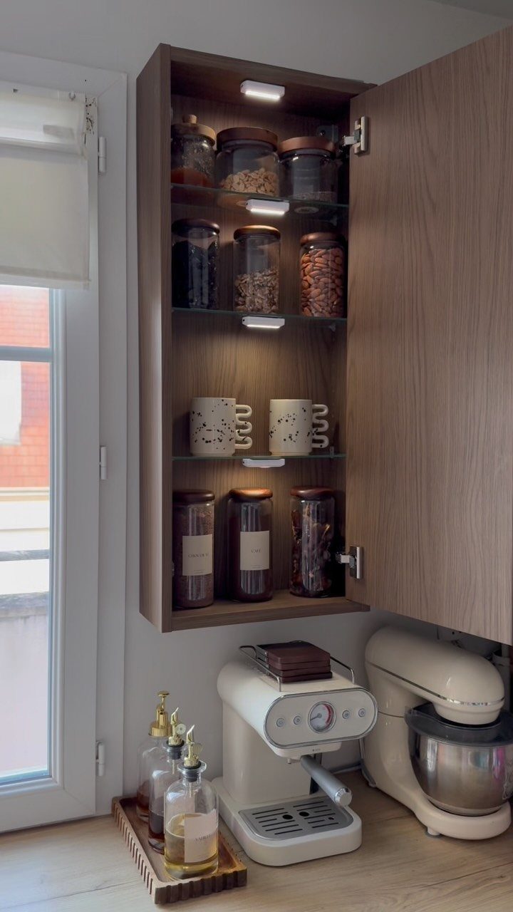 Wooden wall cabinet with coffee supplies above a white espresso machine and mixer.