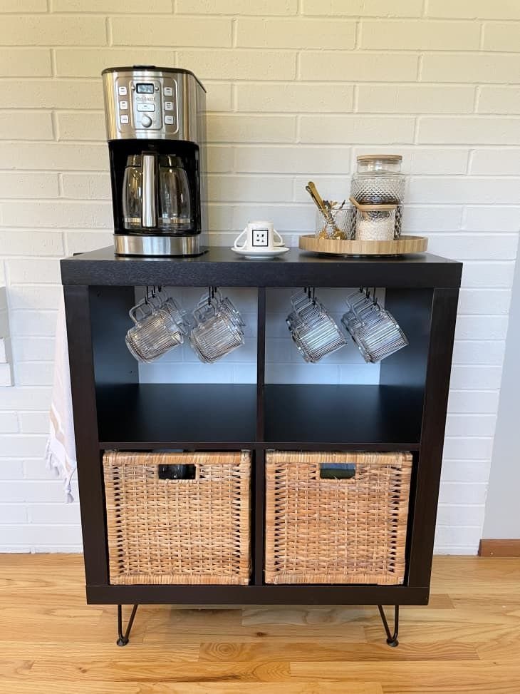Dark brown coffee cabinet with coffee maker, hanging mugs, and wicker storage baskets.