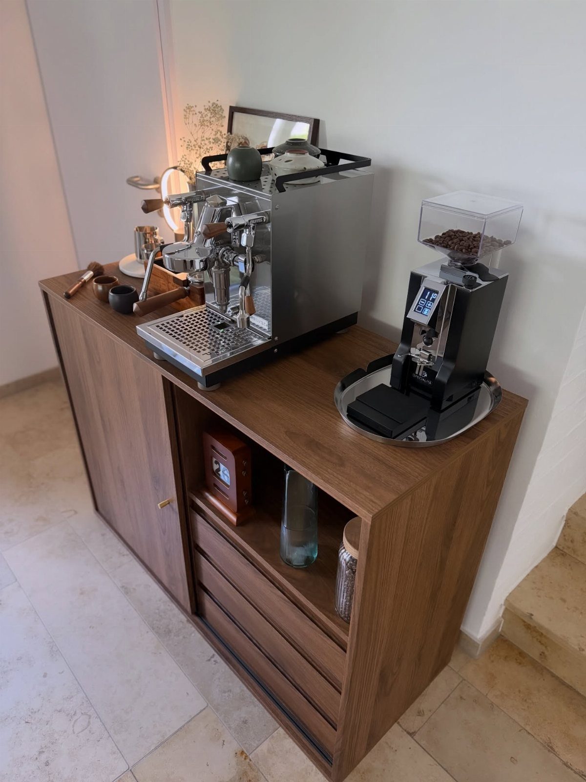Brown wood coffee cabinet holding an espresso machine and grinder against a white wall.