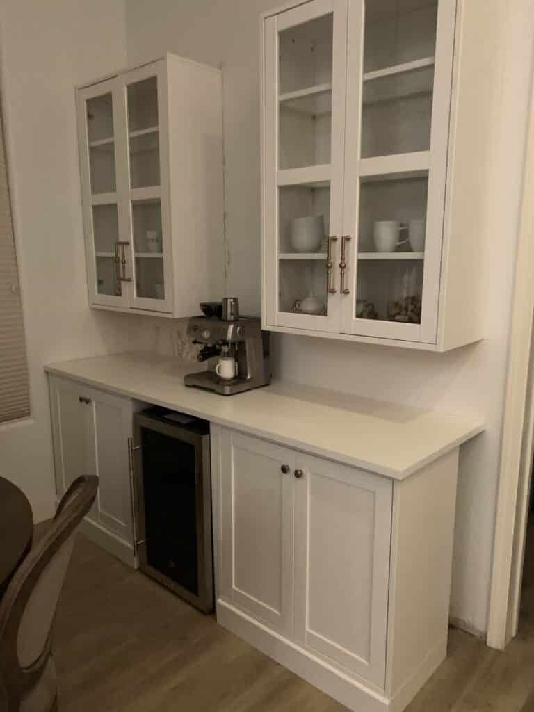White coffee station with glass-front cabinets, espresso machine, and a small wine fridge.