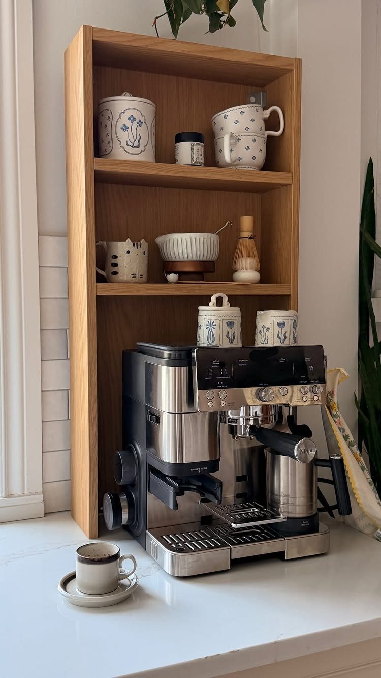 Light wood wall cabinet coffee nook with espresso machine and ceramic mugs on white countertop