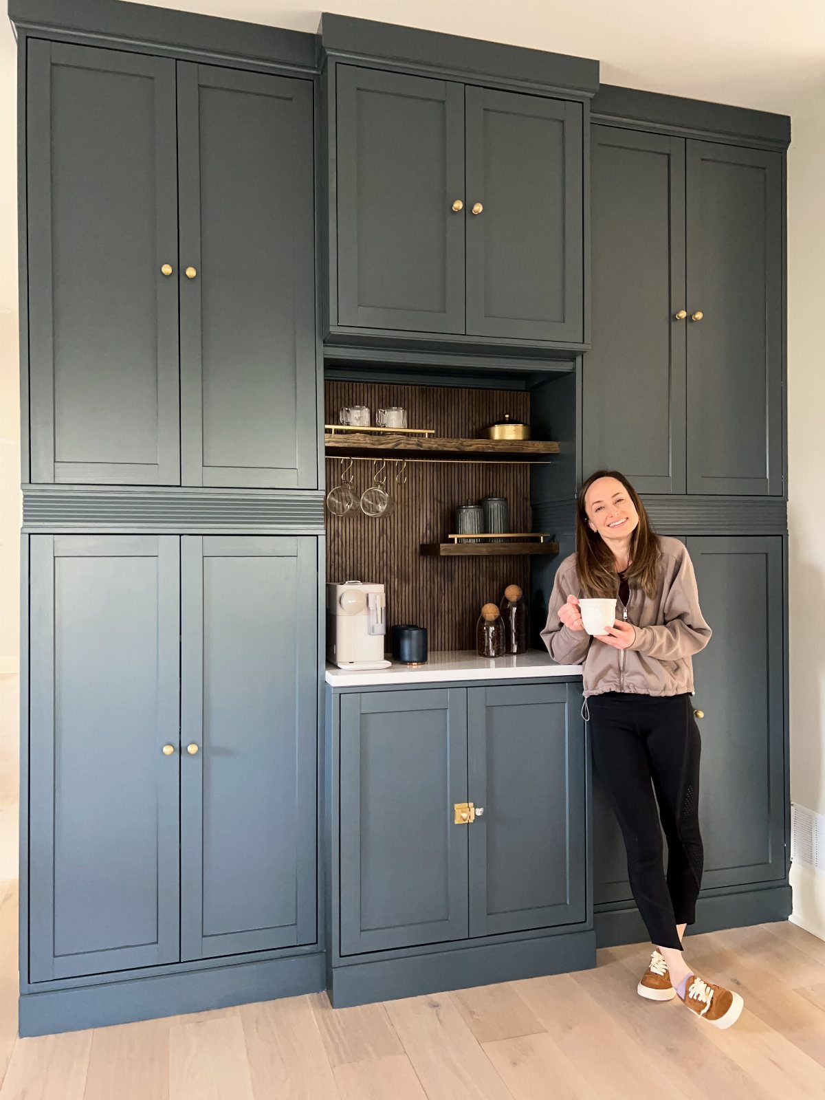 Woman standing by a dark grey-blue IKEA Havsta coffee nook with gold hardware.