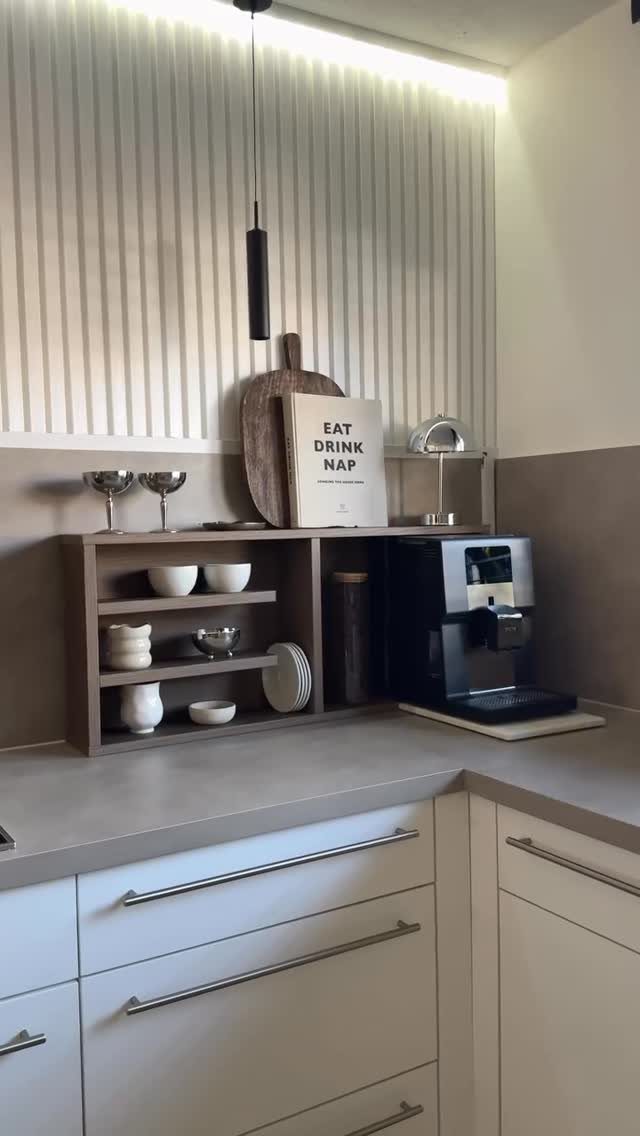 Black espresso machine on a grey counter with slatted wall and wooden shelves.