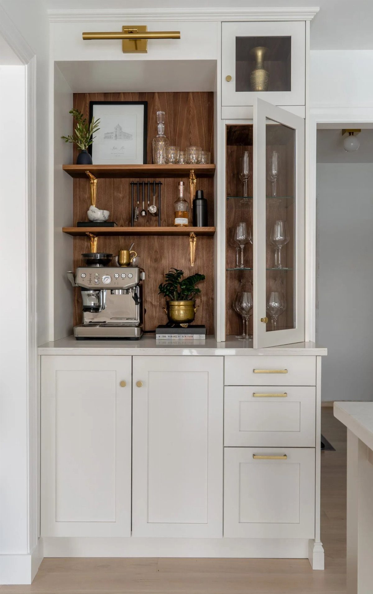 White coffee bar cabinet with walnut wood accents, floating shelves, and an espresso machine.