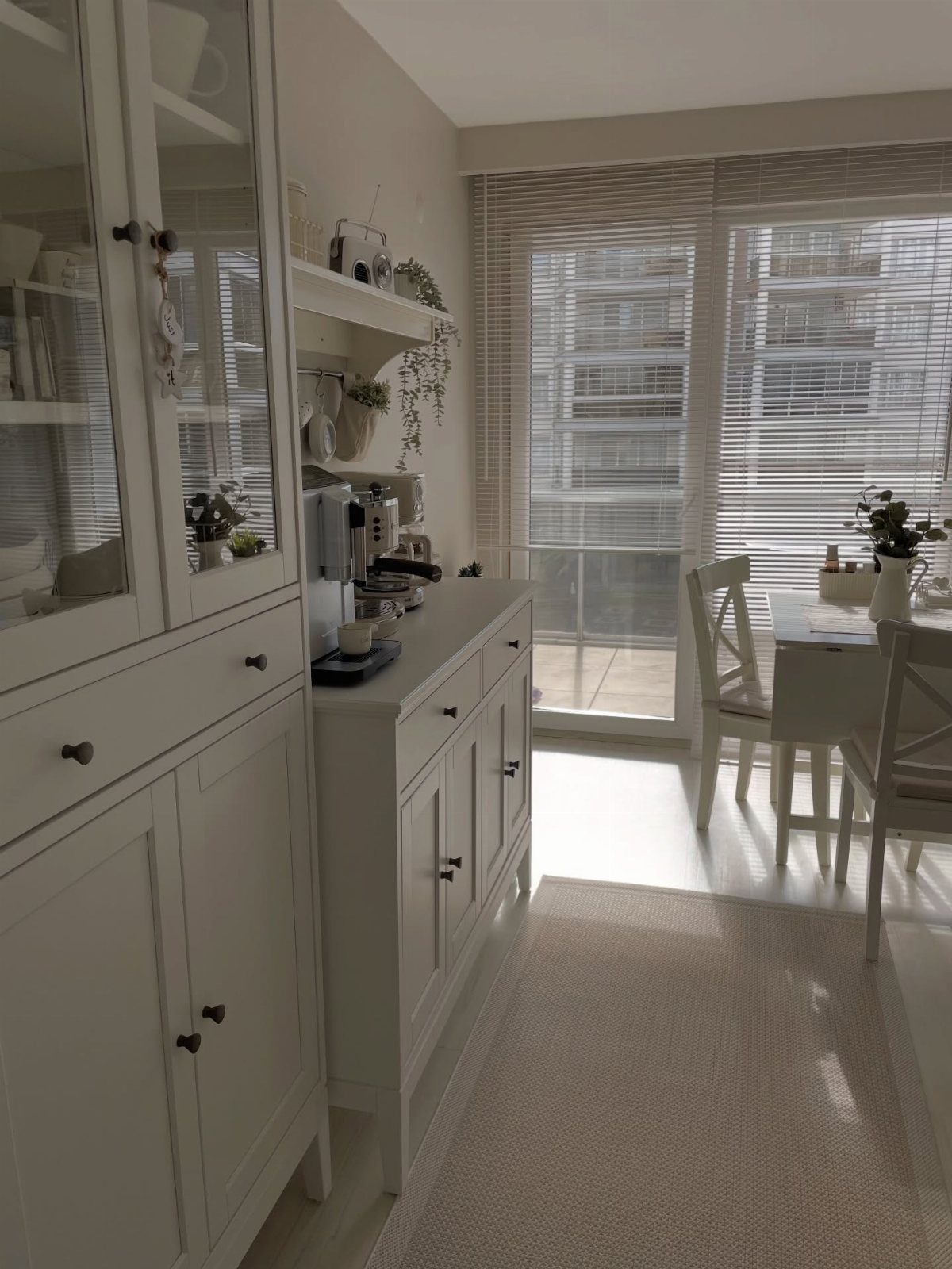 White IKEA coffee cabinet setup with a coffee machine and dining area background.
