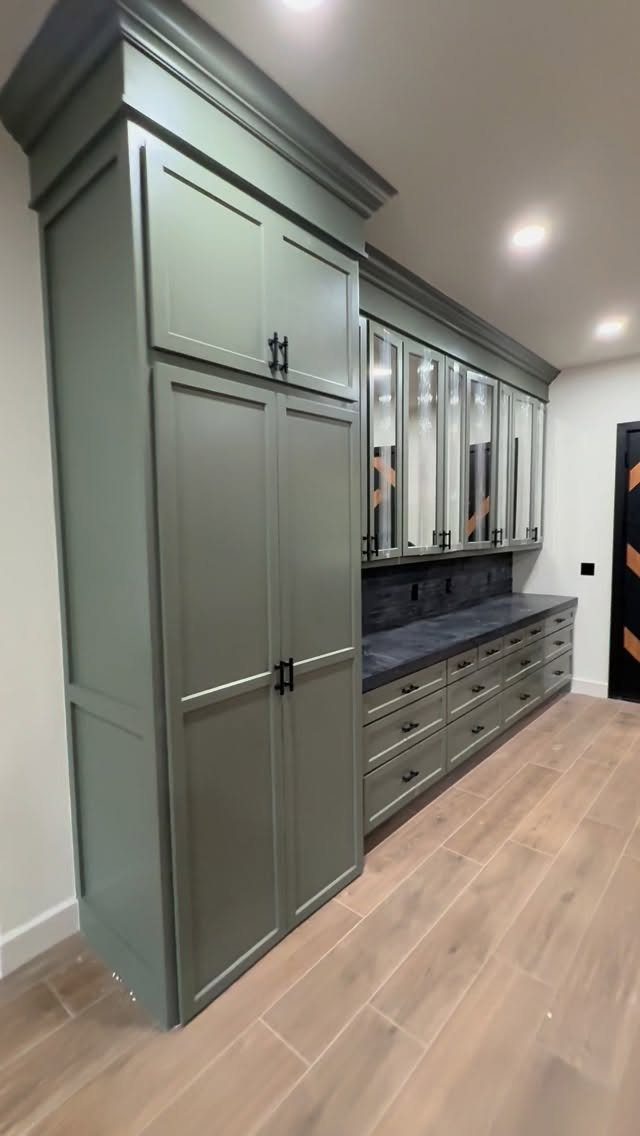 Sage green built-in kitchen pantry cabinet and storage area with light wood floors.