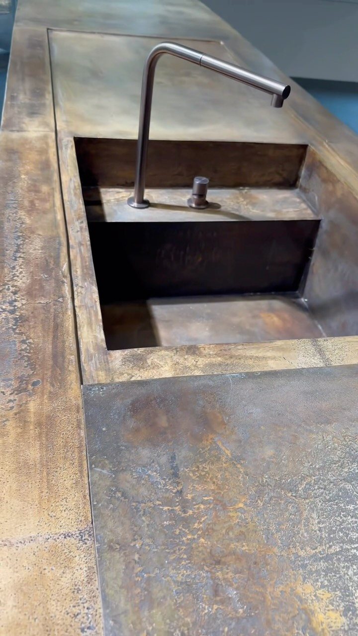 Metallic bronze kitchen island countertop with an integrated sink and matching slim faucet.