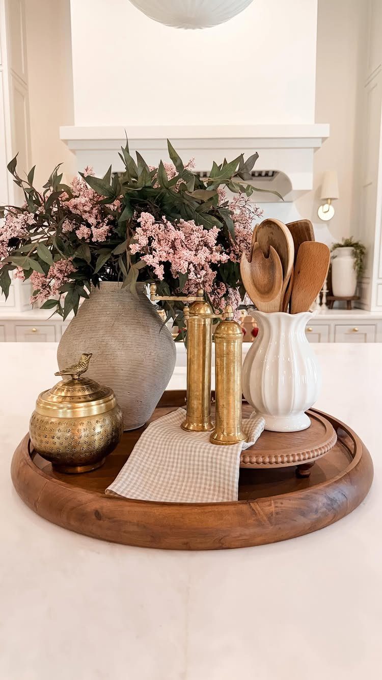 Wooden tray with pink flowers, gold canisters, and wooden spoons on a white counter.