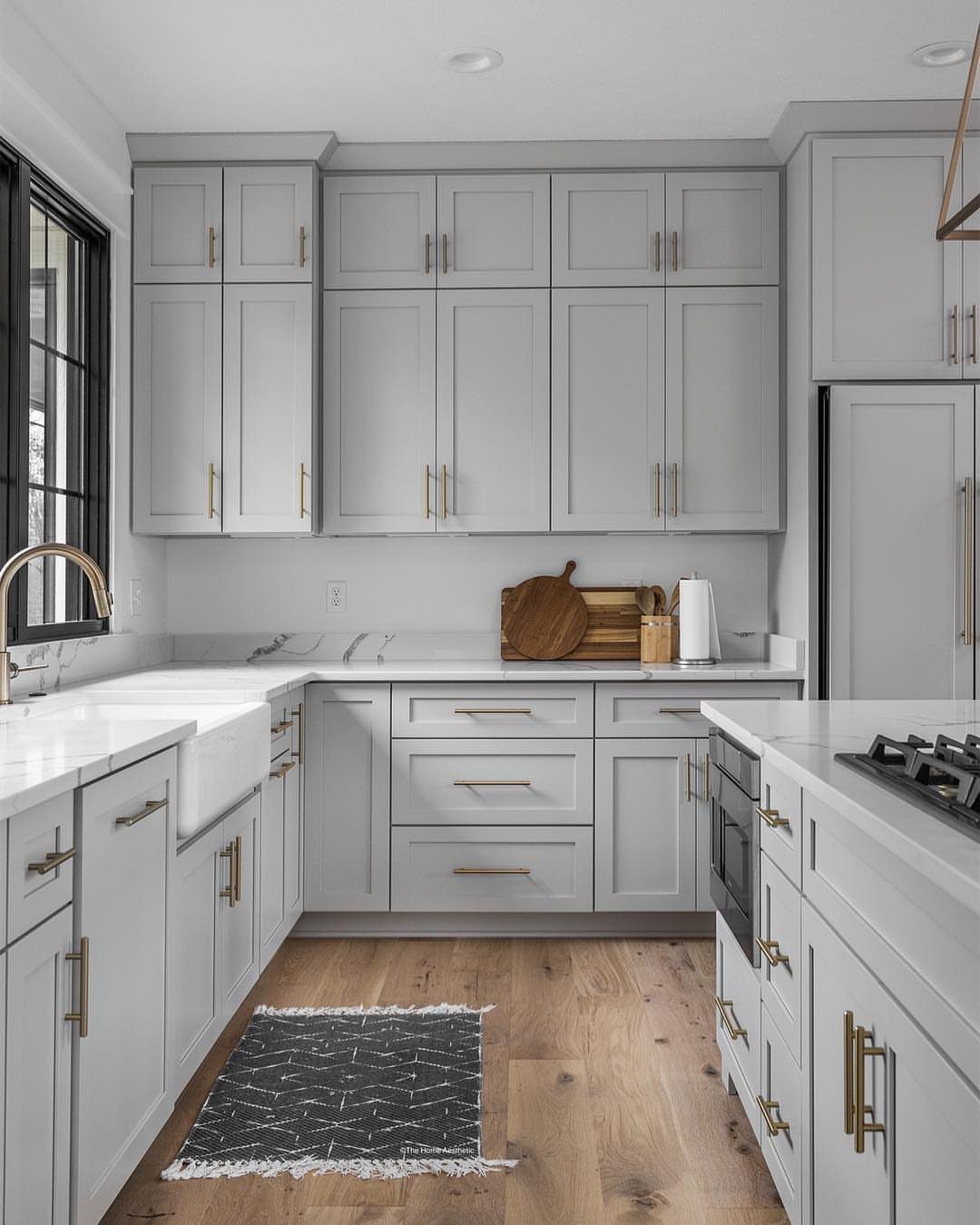 Light grey kitchen cabinets with white marble countertops and light wood flooring.