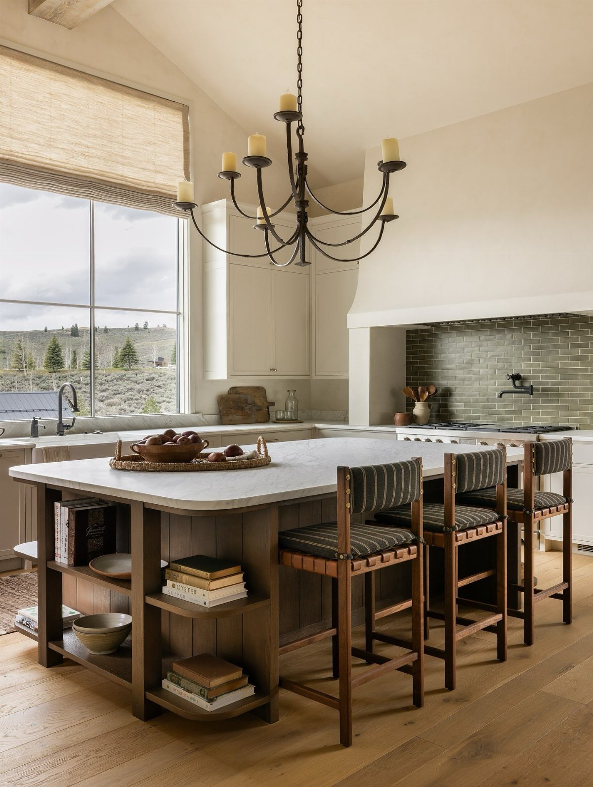 Large white marble kitchen island with wooden shelving and three matching bar stools.