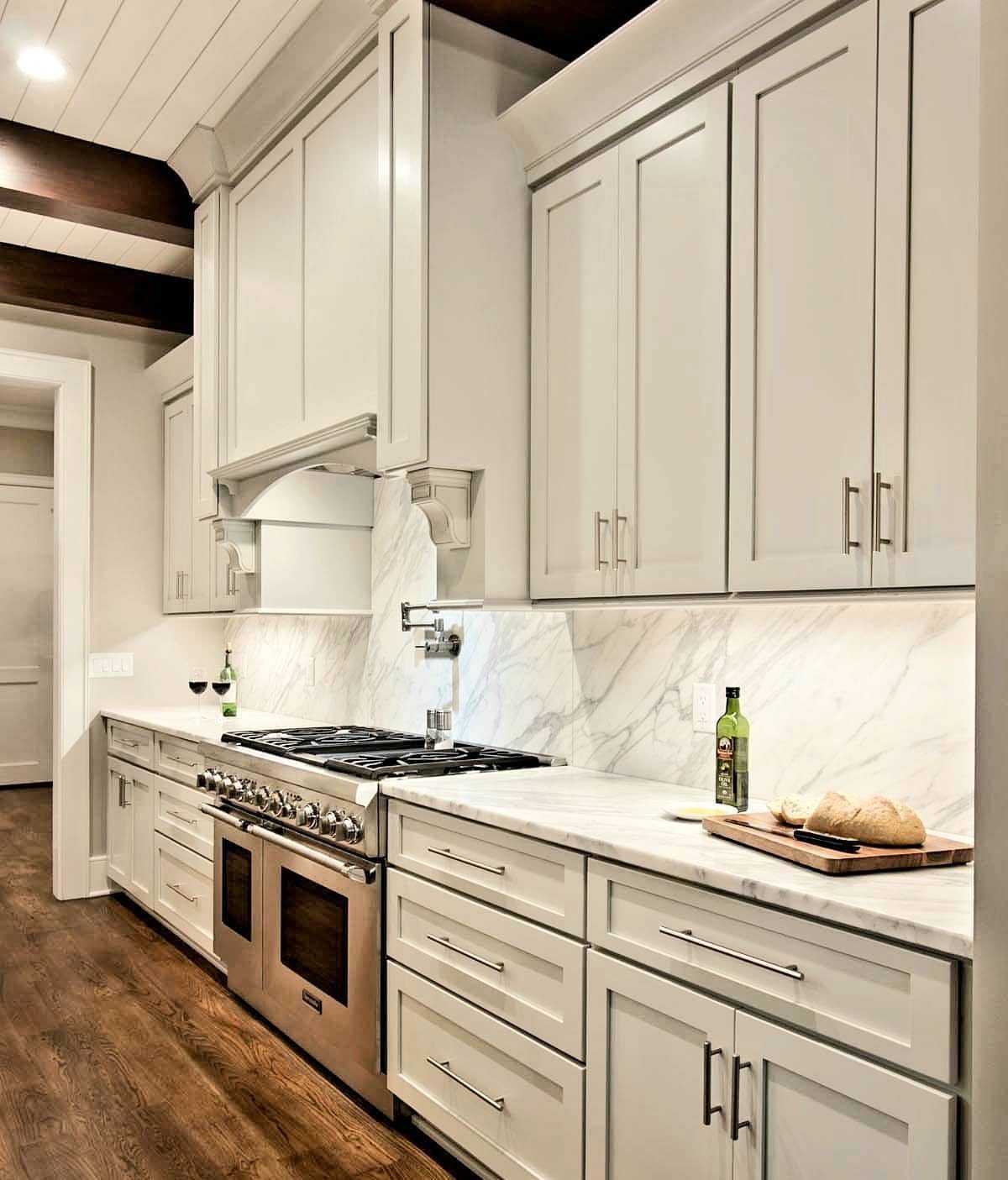 White kitchen with marble countertops, matching backsplash, and stainless steel appliances.