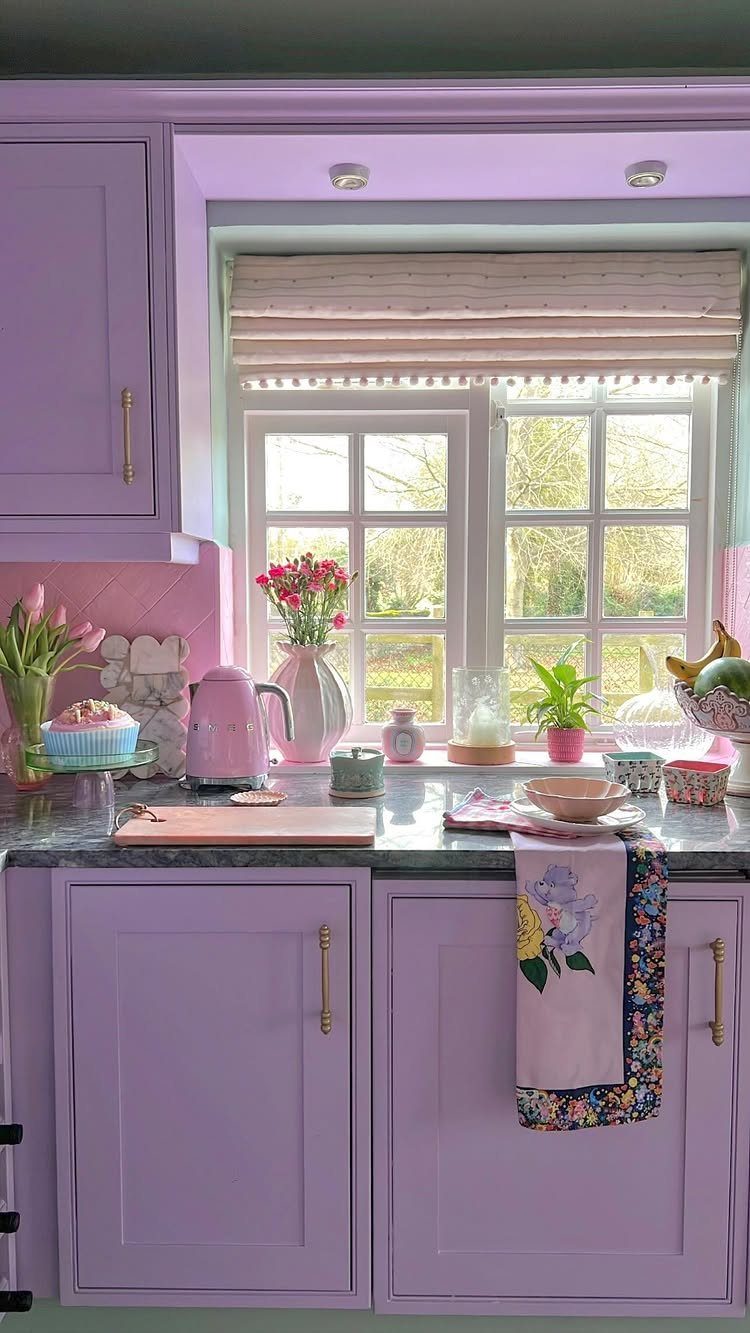 Light purple kitchen cabinets with a grey countertop and a window with flowers.