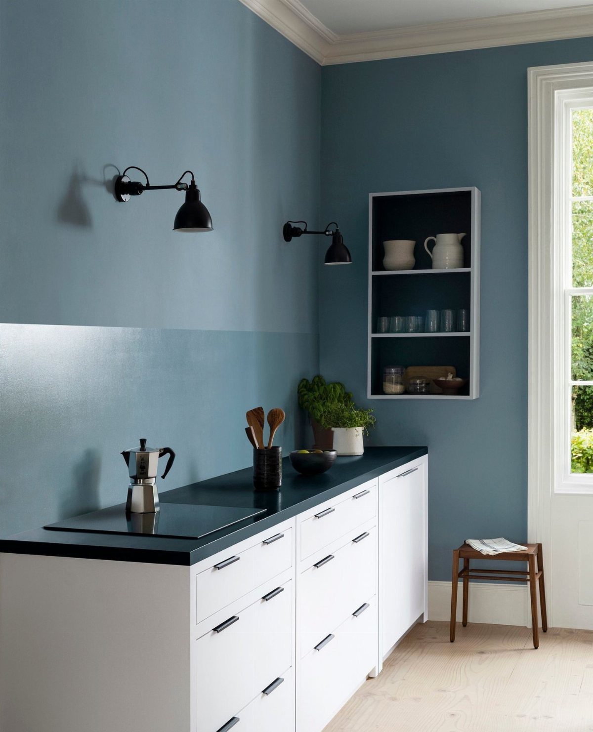 Blue painted kitchen walls with white cabinets, black countertops, and black wall lamps.