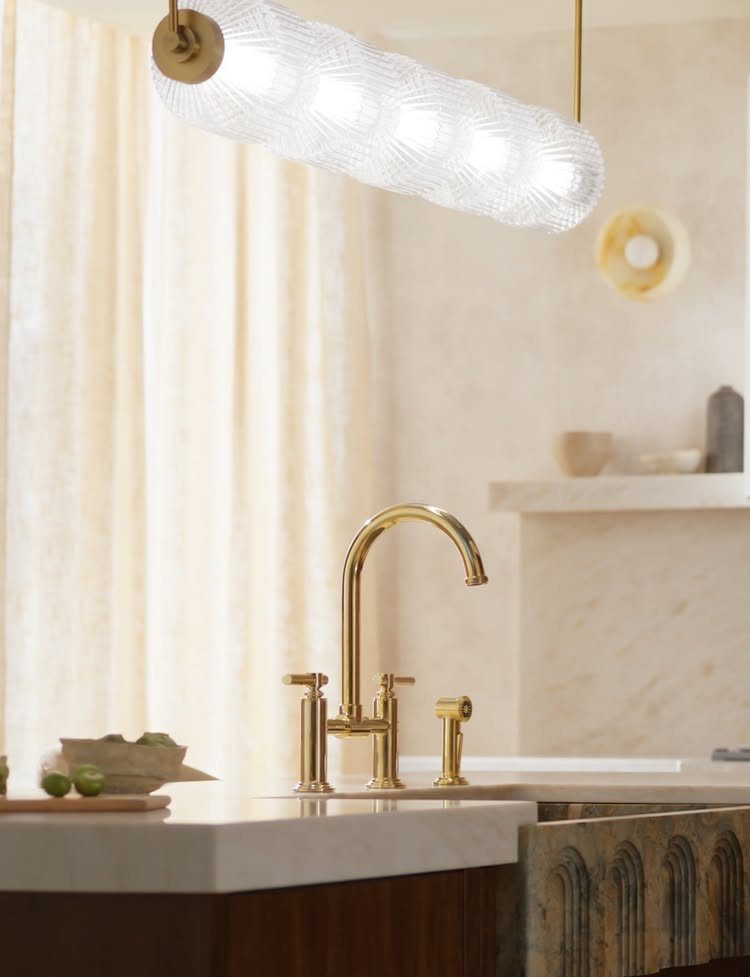 Gold kitchen faucet on a white countertop with a textured glass pendant light above