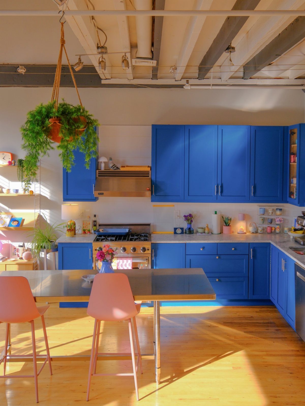 Vibrant blue kitchen cabinets with a stainless steel stove and pink dining chairs.