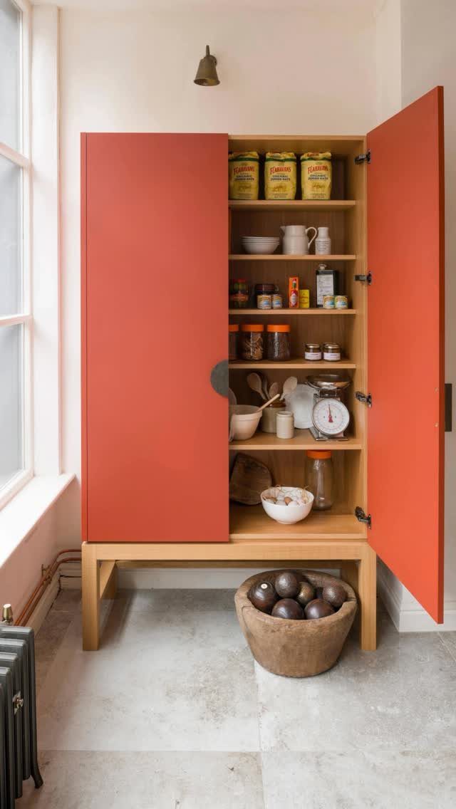 Orange freestanding kitchen cabinet with open doors and a wooden bowl on the floor.