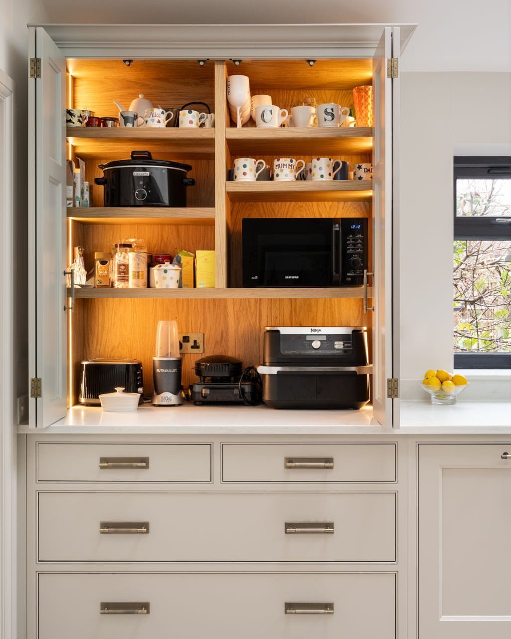 Kitchen cabinet with built-in lighting storing a microwave, toaster, and other small appliances.