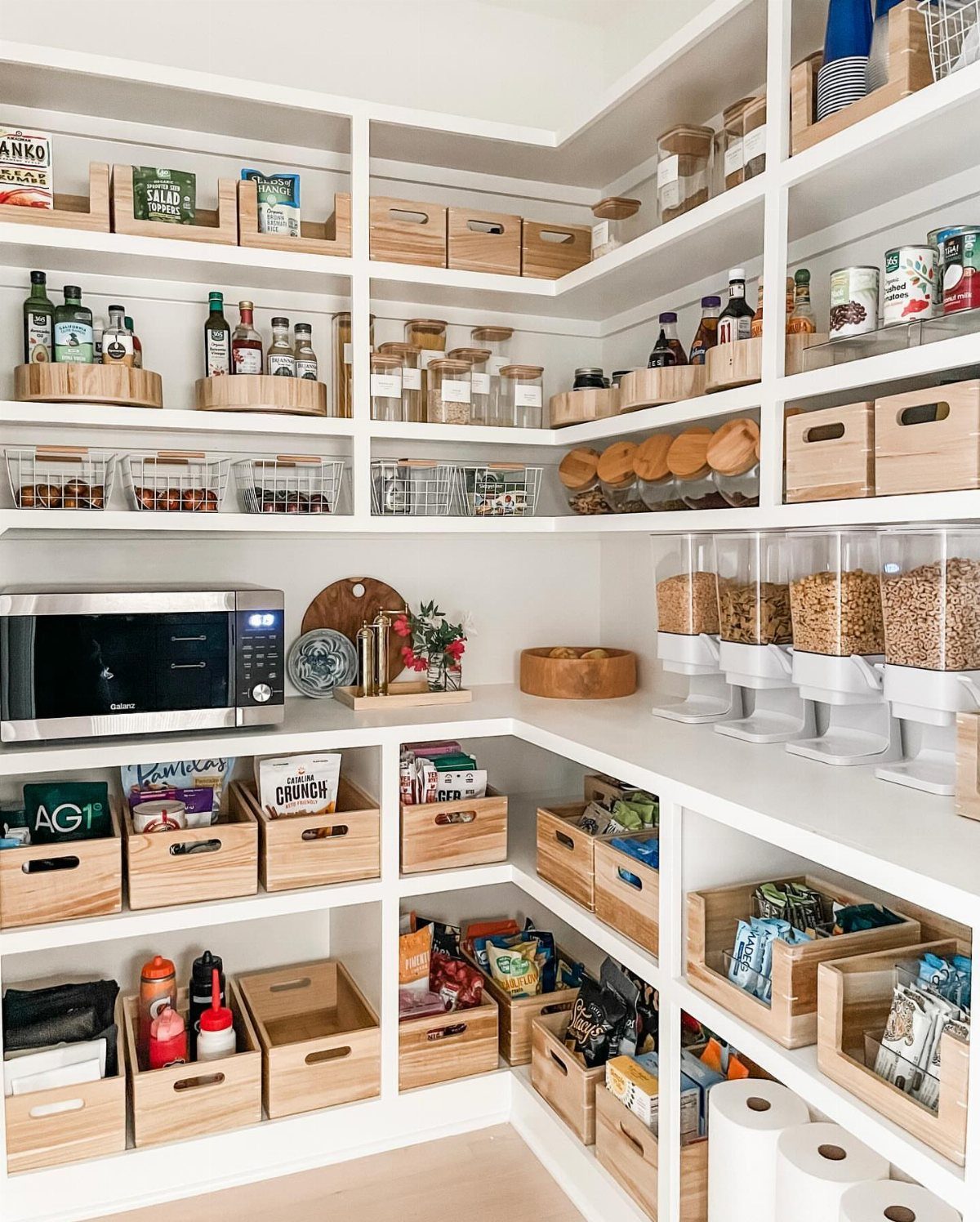 White pantry shelves with wooden bins and clear cereal dispensers containing grains.