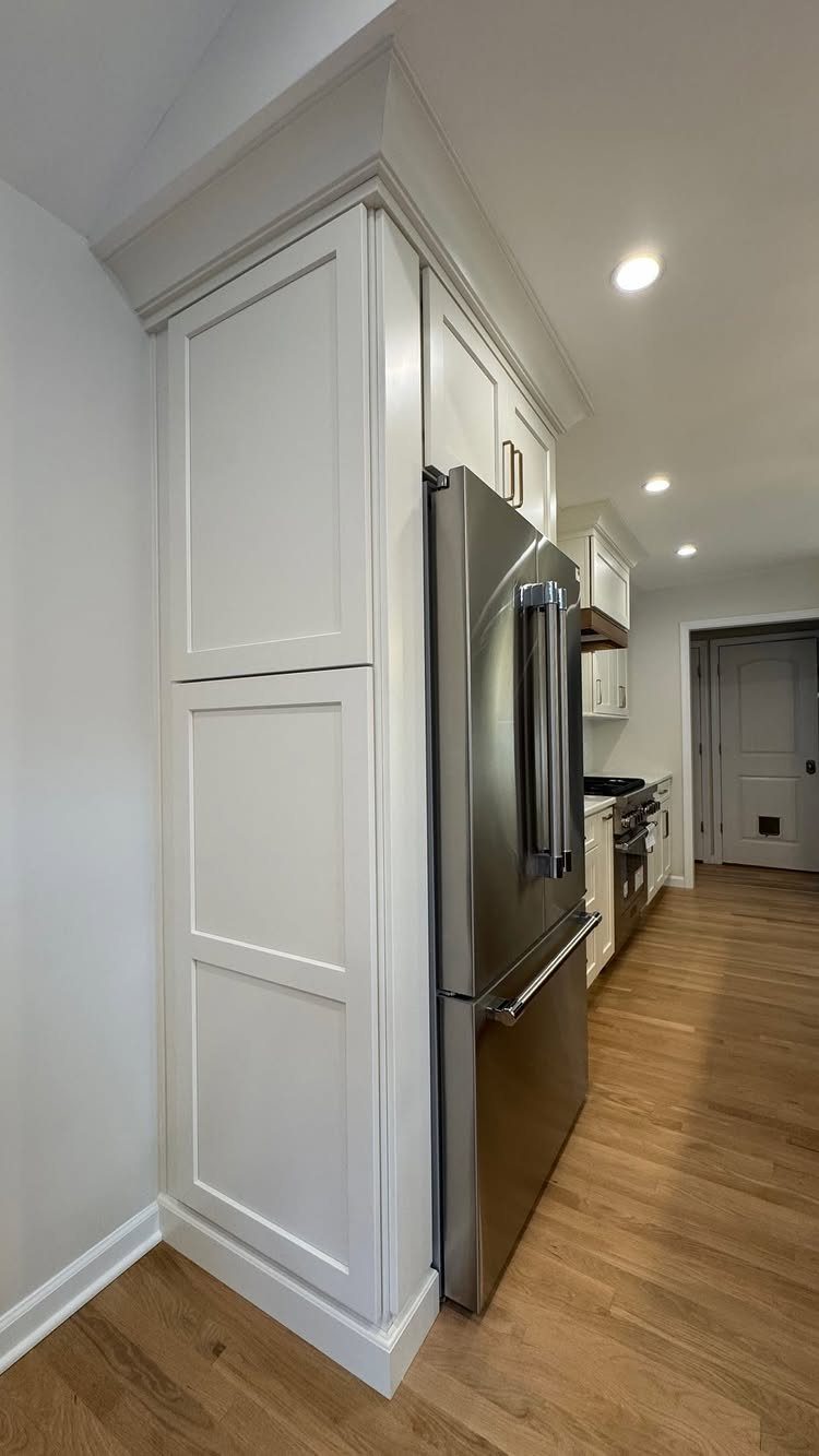 Stainless steel refrigerator with a white storage cabinet installed above it in a kitchen.