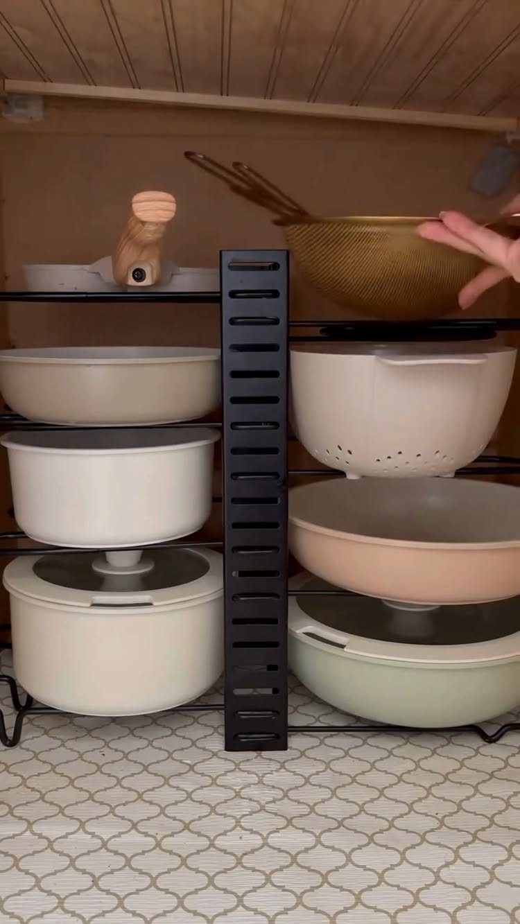 Pots and pans organized on black wire racks inside a kitchen cupboard.