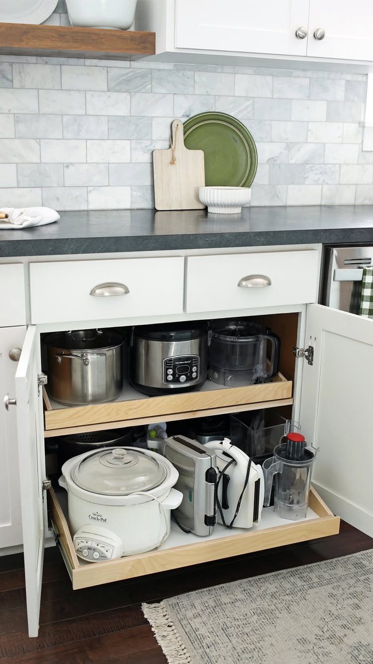 Wooden pull-out shelves in a white kitchen cabinet holding various small kitchen appliances.