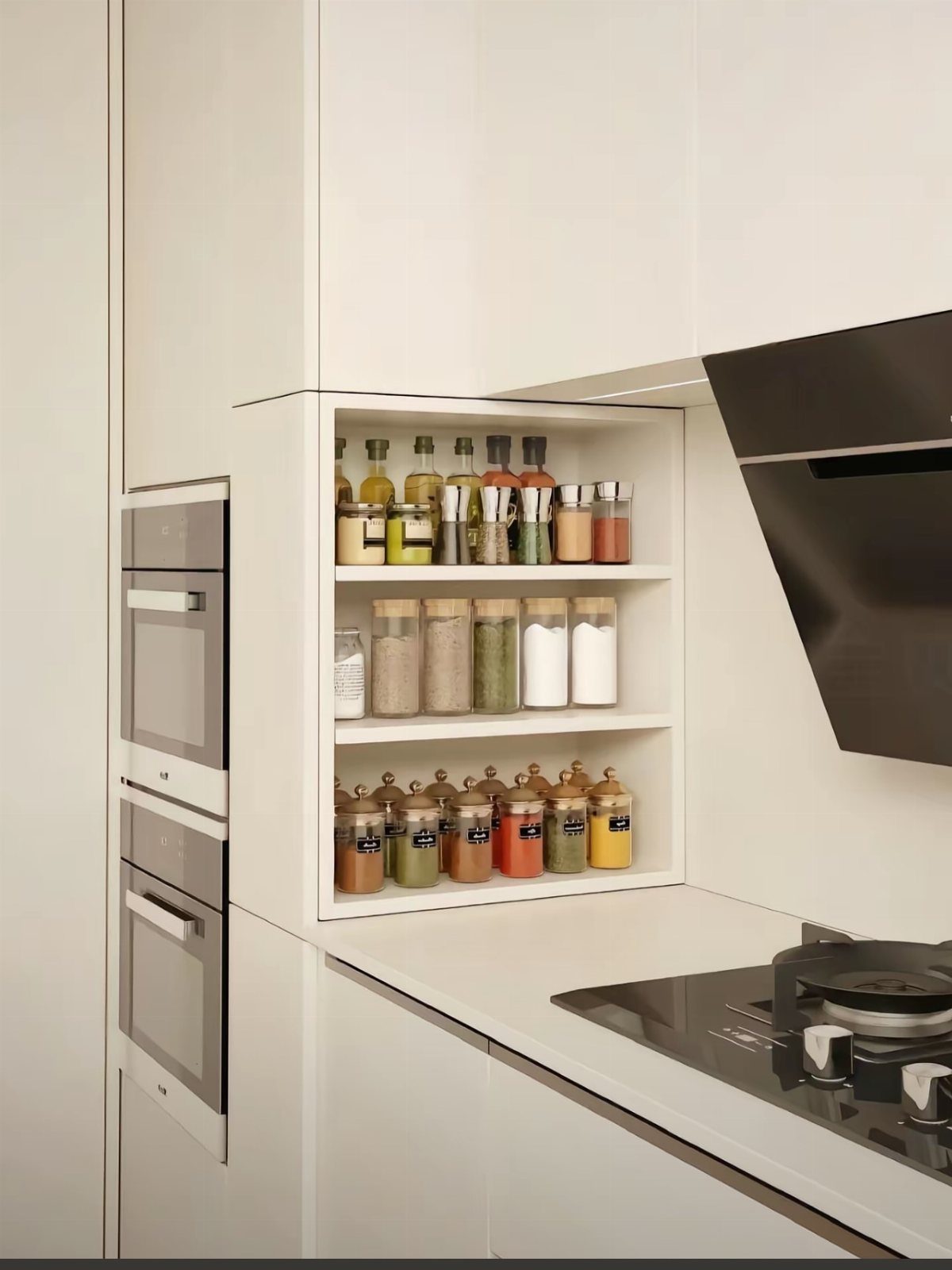 White built-in kitchen spice rack with organized jars and bottles next to an oven.