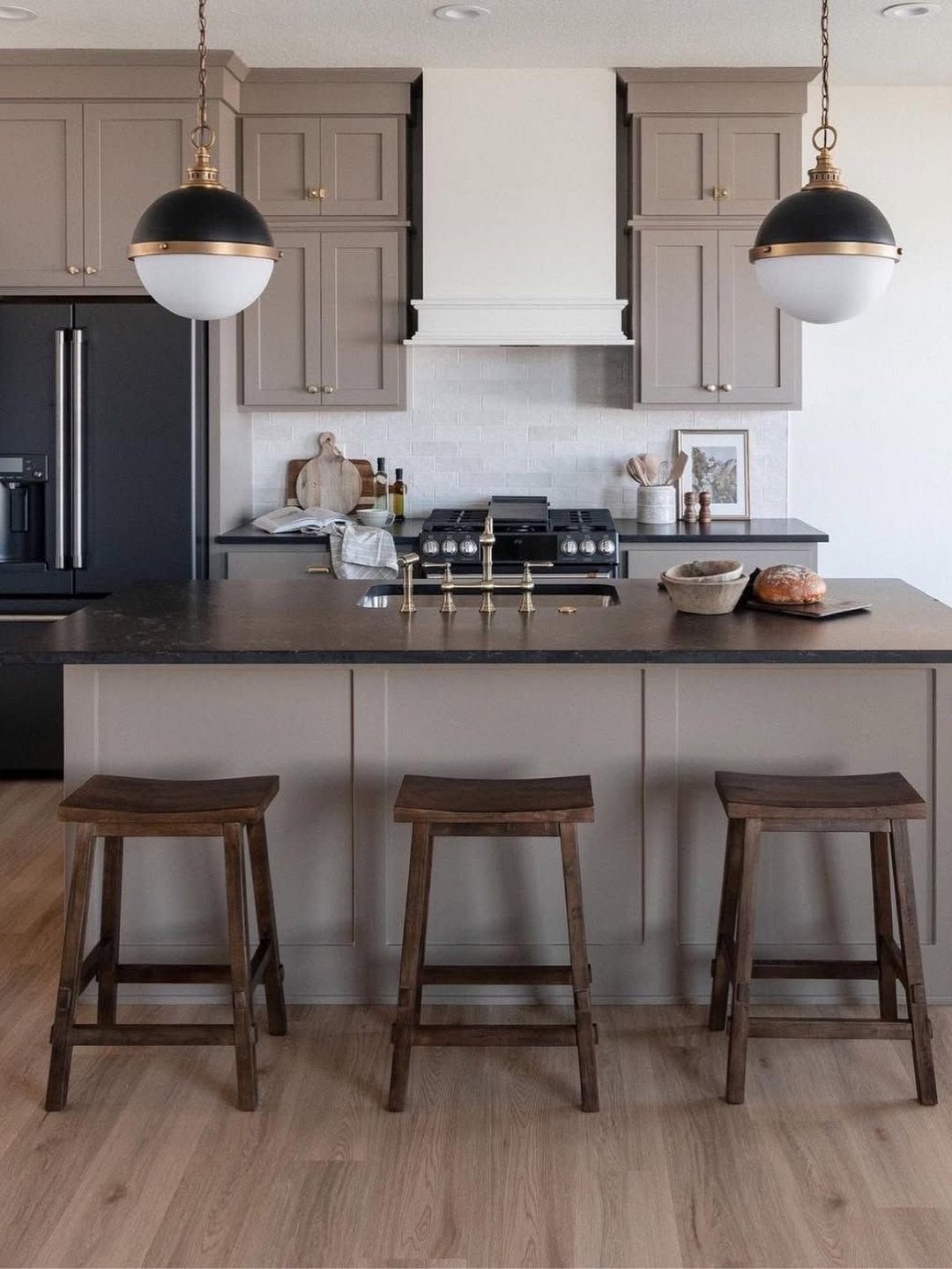 Taupe kitchen cabinets and dark island with wooden stools and globe pendant lights.