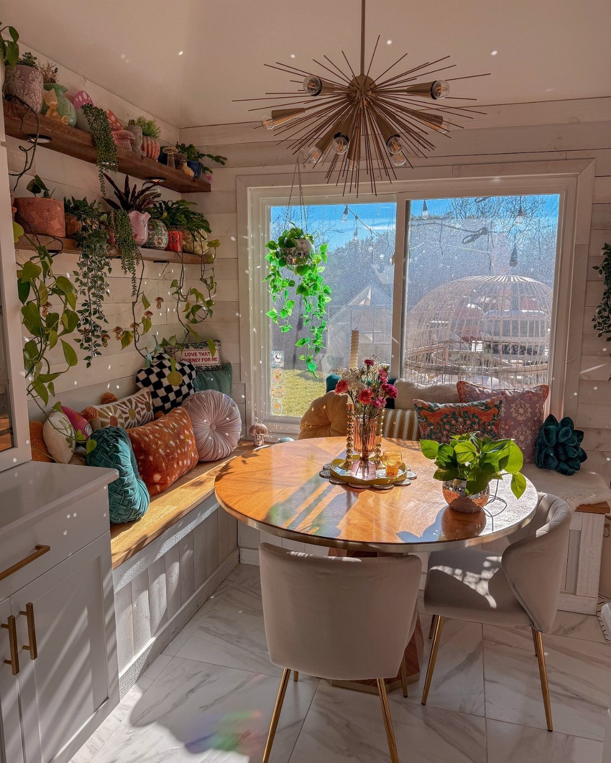 Kitchen nook with a round wooden table and window seat overlooking a snowy scene.
