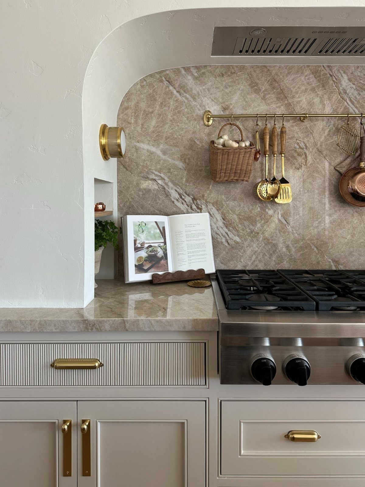 Kitchen stove and vent hood set within a white arched architectural alcove.