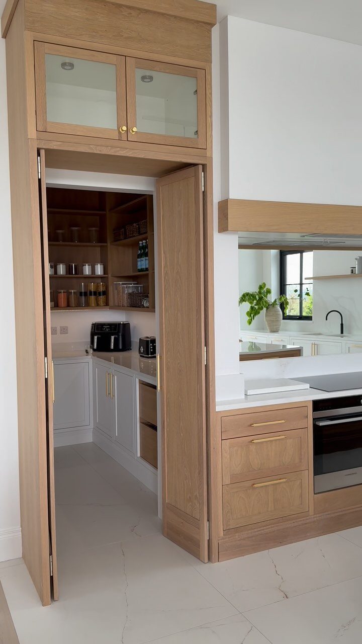 Walk-in pantry with wooden shelving and white cabinets accessed through a light wood door.