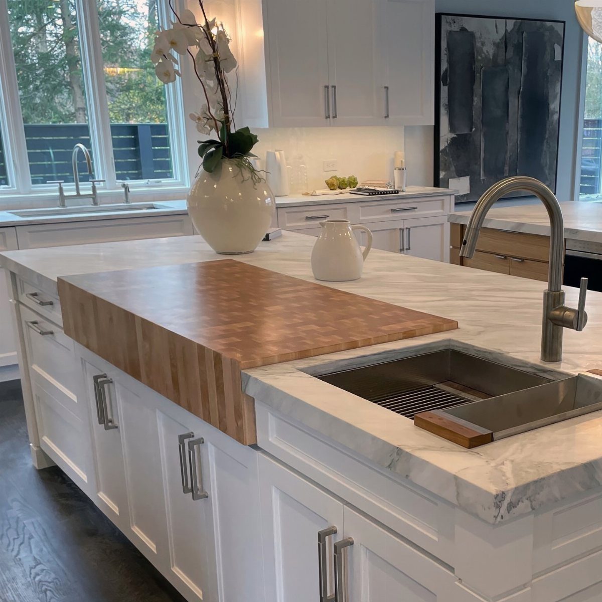 White kitchen island with marble countertop and integrated wooden butcher block prep surface.