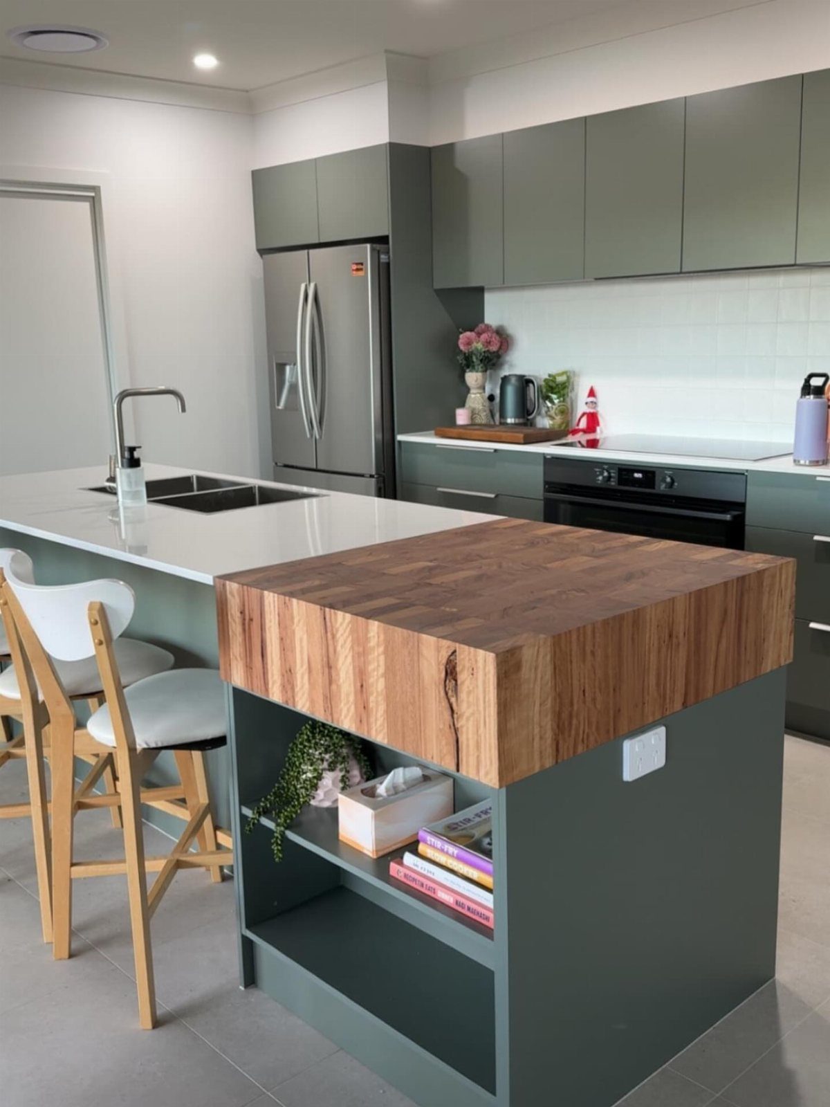 Green kitchen island with a thick wooden butcher block top and open shelving.