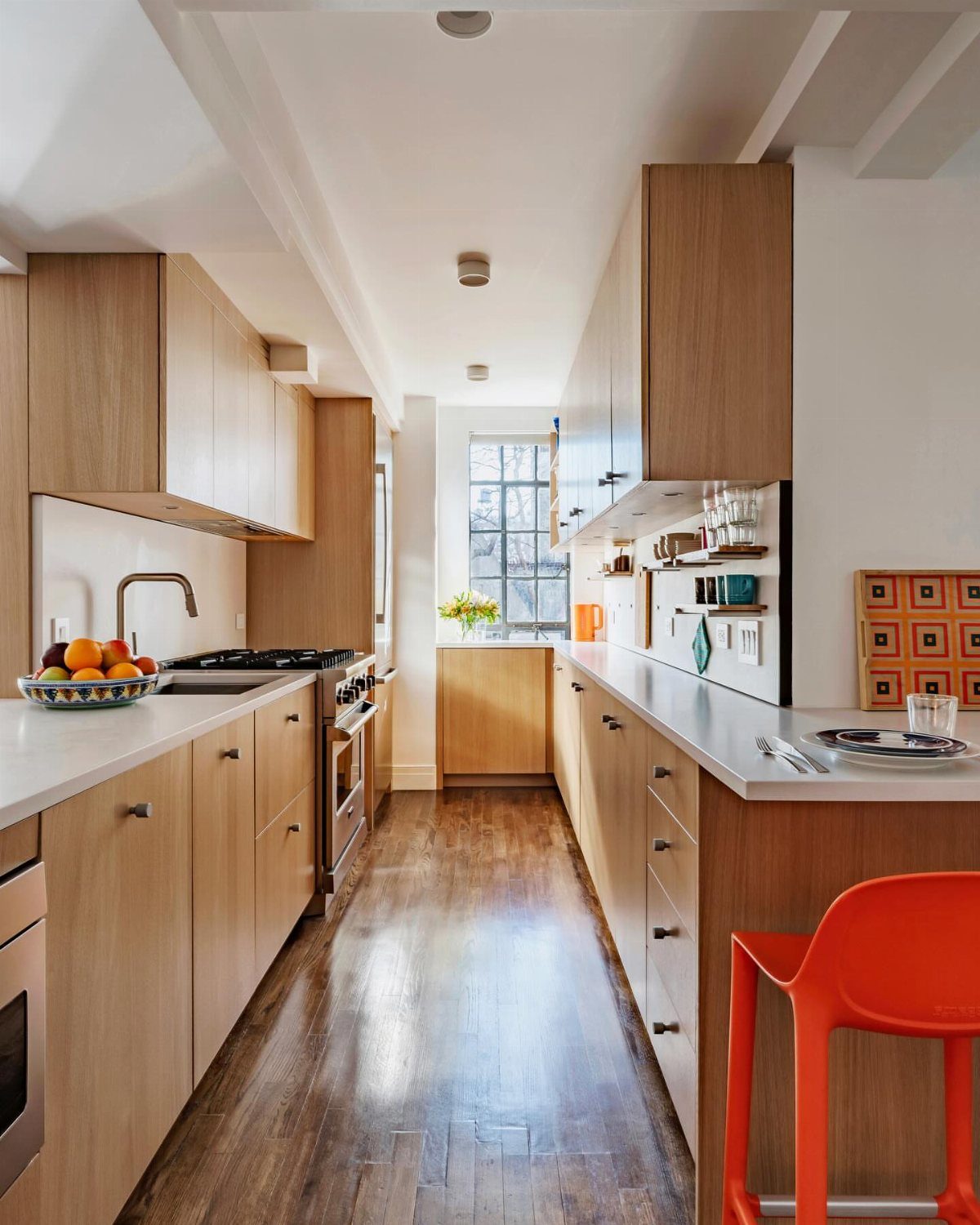 Galley kitchen with parallel light wood cabinets, white countertops, and dark wood flooring.