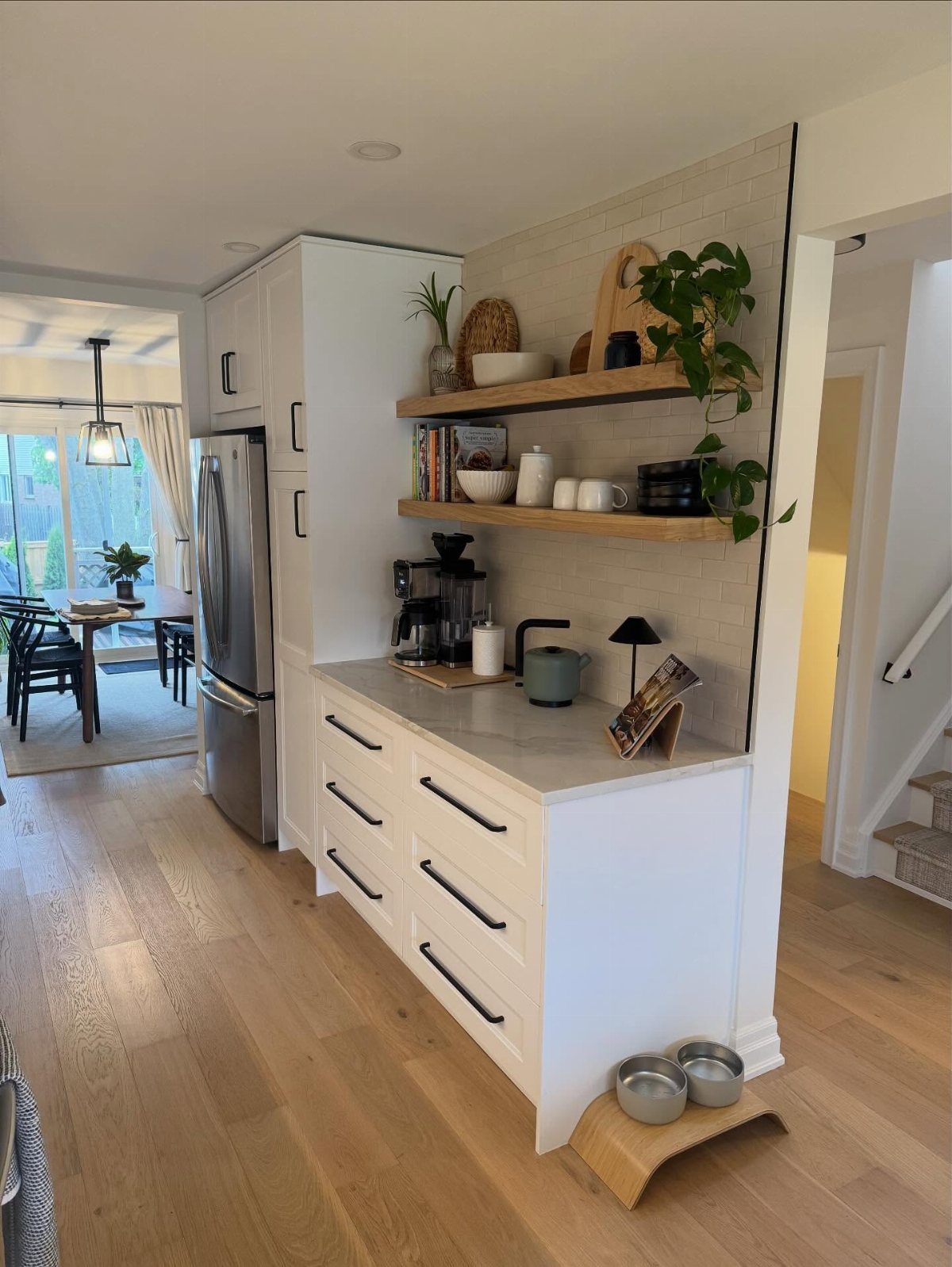 White kitchen half island with grey countertop, open wooden shelves, and coffee station.